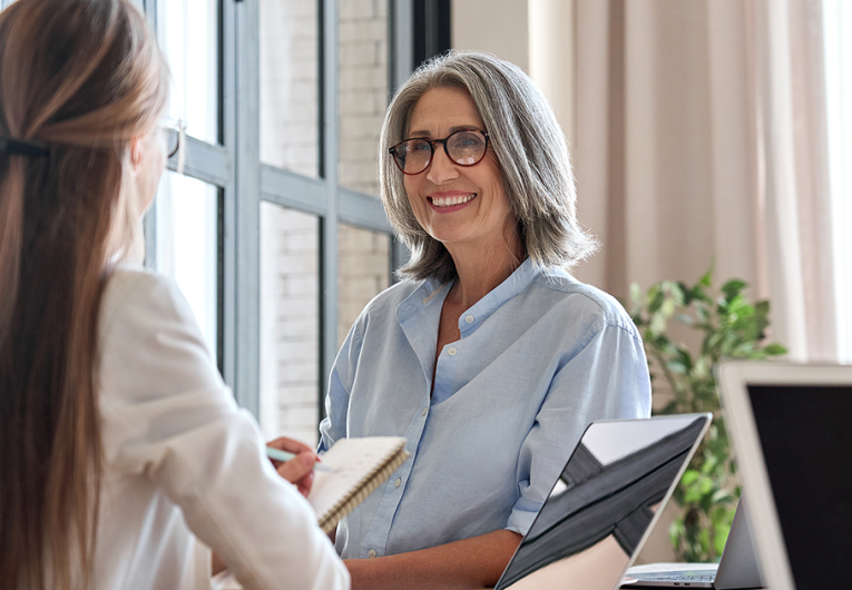 Happy mature businesswomen talking to colleague in meeting working together in office