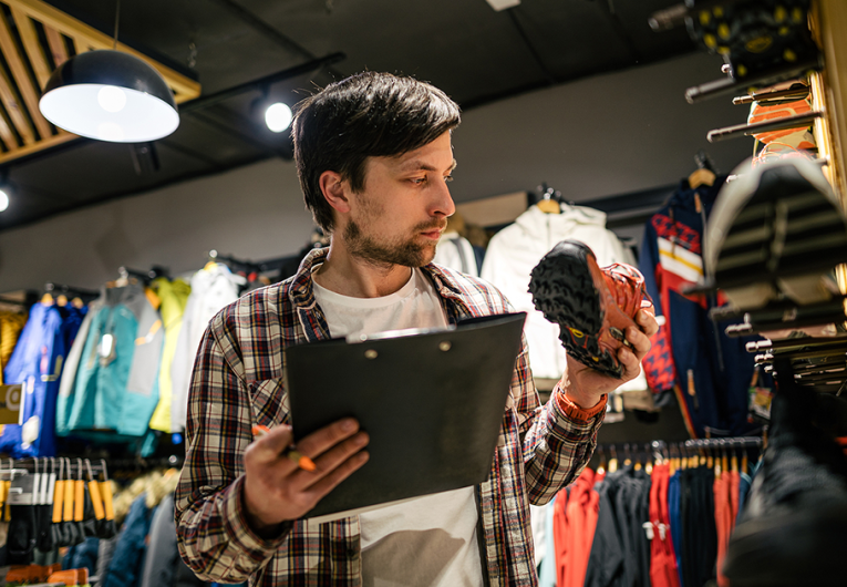 Store manager near shelves with hiking boots makes check list